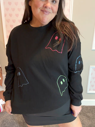 Person wearing a black sweatshirt with colorful ghost designs in a room.