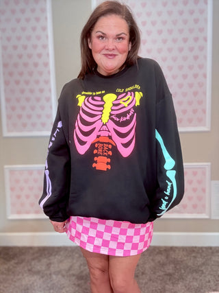 Person wearing a black sweatshirt with colorful skeleton design and a pink checkered skirt in a room with heart-patterned wallpaper.