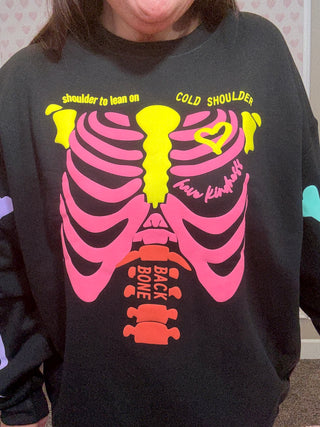 Black sweatshirt with colorful skeleton design and text worn by a person.