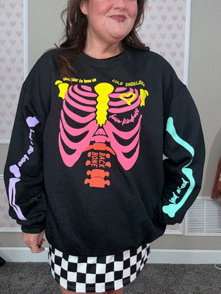 Person wearing a black sweatshirt with colorful skeleton design in front of a heart-patterned wall.