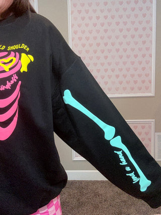 Black sweatshirt with pink skeleton design and text on sleeve, worn by a person.