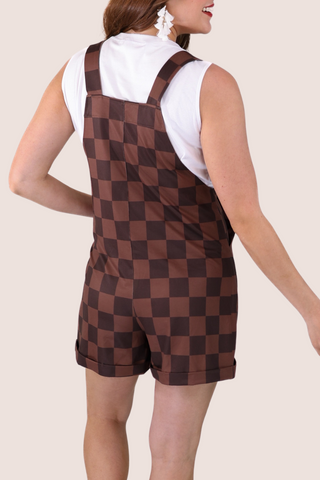 Person wearing a brown checkered romper with a white shirt underneath on a beige background