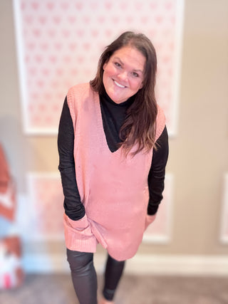 Woman wearing a pink vest over a black long-sleeve shirt with a blurred background