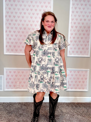 Woman wearing a western patterned dress with black boots in front of heart-themed wallpaper.