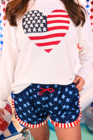 Person wearing a white sweatshirt with an American flag design and blue shorts with star pattern.