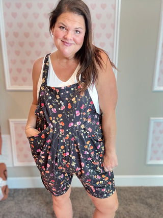 Woman wearing a floral romper in a room with heart-patterned wallpaper.