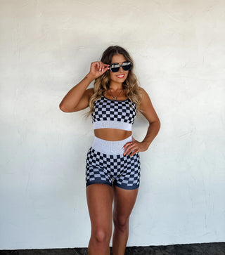 Model wearing a two-tone checkered ribbed seamless workout set with scoop neck bra and high-waisted biker shorts in a bold black and beige check pattern