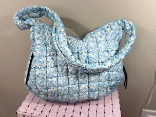 Blue Ditsy Floral Quilted Bag with a charming floral print, secure zipper closure, water-resistant inner lining, multiple pockets, and a comfortable shoulder strap—perfect for everyday use or travel.