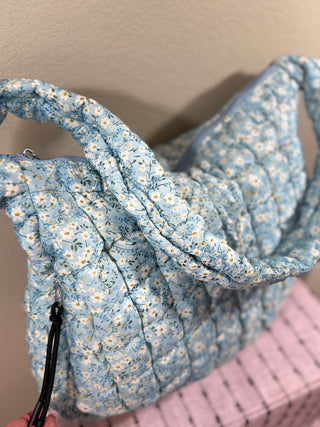 Blue Ditsy Floral Quilted Bag with a charming floral print, secure zipper closure, water-resistant inner lining, multiple pockets, and a comfortable shoulder strap—perfect for everyday use or travel.
