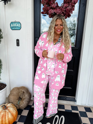 Woman wearing pink ghost-themed pajamas standing in front of a door with pumpkins and a wreath.