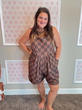 Woman wearing a checkered romper standing in a room with heart-patterned wallpaper.