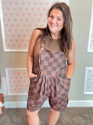 Woman wearing a brown checkered romper in a room with heart-patterned wallpaper.