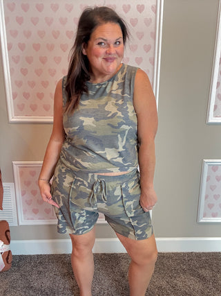 Woman wearing a camouflage outfit standing in a room with heart-patterned wallpaper.