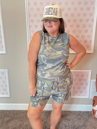 Person wearing a camouflage outfit and 'GAMEDAY' cap in a room with heart-patterned wallpaper.
