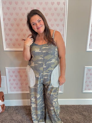 Woman wearing a camouflage outfit in a room with heart-patterned wallpaper.