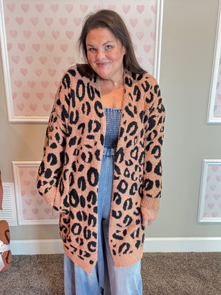 Woman wearing a leopard print cardigan in a room with heart-patterned wallpaper.