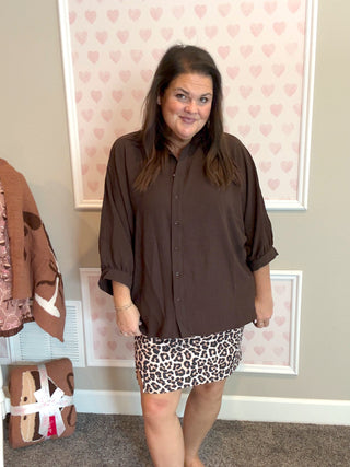 Woman wearing a brown shirt and leopard print skirt in a room with heart-patterned wallpaper.