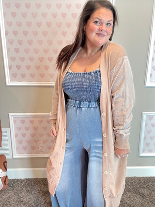 Woman wearing a beige cardigan over a blue outfit in a room with heart-patterned wallpaper.