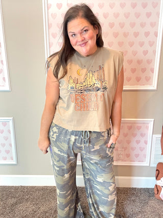 Woman wearing a graphic t-shirt and camouflage pants in a room with heart-patterned wallpaper.