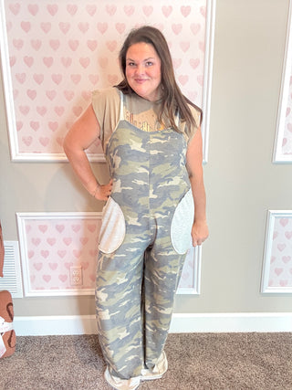 Woman wearing a camouflage jumpsuit with heart-patterned wallpaper in the background