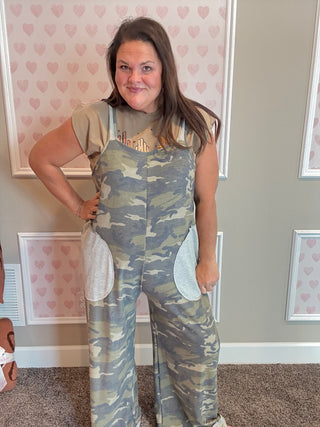 Woman wearing camouflage overalls in a room with heart-patterned wallpaper.