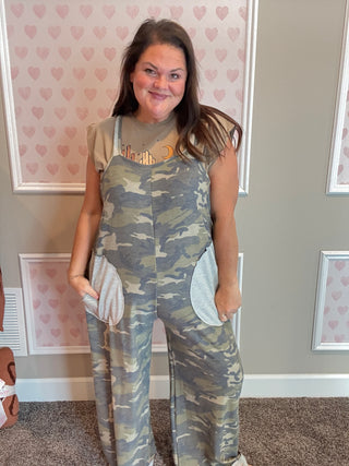 Woman wearing camouflage overalls in a room with heart-patterned wallpaper.