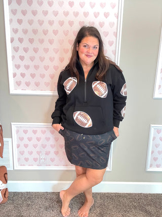 Woman wearing a black hoodie with football designs in a room with heart-patterned wallpaper.