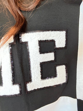 Close-up of black and white color block tee with sequin-outlined football patch, ideal for casual team spirit looks.