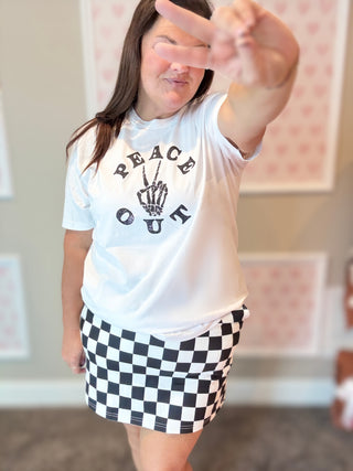 Person wearing a white t-shirt with 'Peace Out' graphic and a black and white checkered skirt.