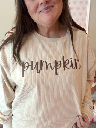 Person wearing a beige ribbed long-sleeve shirt with 'pumpkin' text.