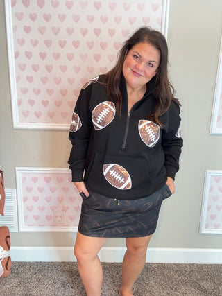 Woman wearing a black hoodie with football designs in a room with heart-patterned wallpaper.