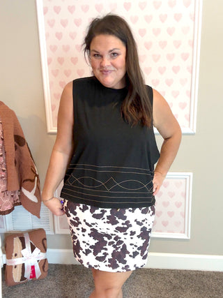 Woman wearing a black sleeveless top and patterned skirt in a room with heart-shaped decorations on the wall.