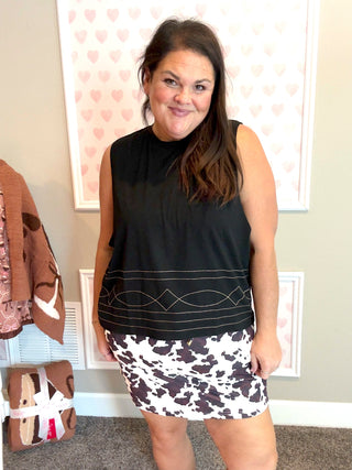 Woman wearing a black sleeveless top and patterned shorts in a room with a heart-themed wall.