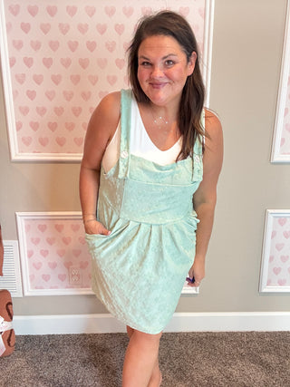 Woman wearing a light green dress with a white top in a room with heart-patterned wallpaper.