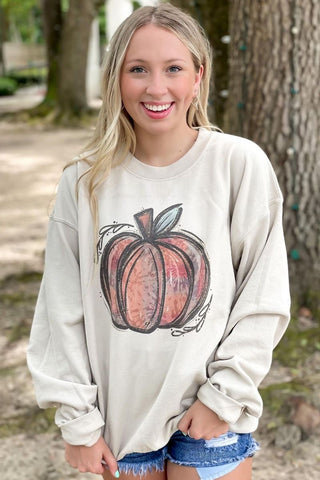 Woman wearing a beige sweatshirt with a pumpkin graphic outdoors.