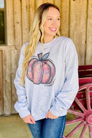 Woman wearing a gray sweatshirt with a pumpkin design in front of a wooden wall.