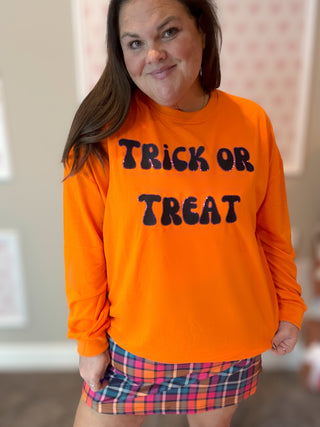 Person wearing an orange 'Trick or Treat' shirt with a plaid skirt.