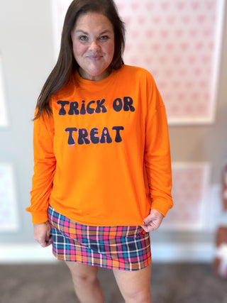 Person wearing an orange 'Trick or Treat' shirt with a plaid skirt indoors.