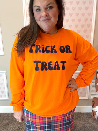 Person wearing an orange 'Trick or Treat' shirt in a room with heart-patterned wallpaper.