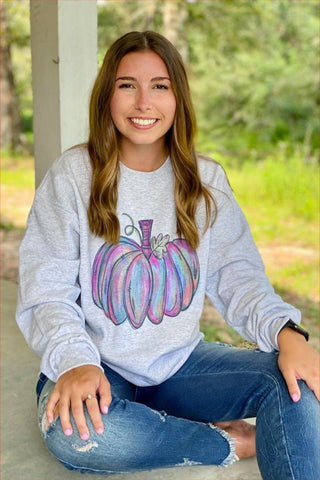 Woman wearing a gray sweatshirt with a colorful pumpkin design, sitting outdoors.
