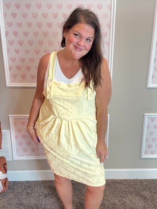 Woman wearing a yellow pinafore dress in a room with heart-patterned wallpaper.