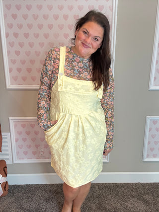 Woman wearing a yellow lace dress with a floral top in a room with heart-patterned wallpaper.