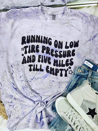 Purple tie-dye shirt with text, jeans, and sneakers on a neutral background.