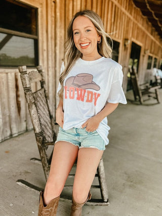 Woman in graphic t-shirt and shorts posing on a rock chair in front of a barn.