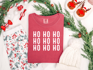 Pink t-shirt with 'HO HO HO' text surrounded by Christmas decorations on a white background