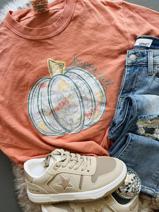 Peach t-shirt with pumpkin design, beige sneaker, and denim jeans on a textured surface
