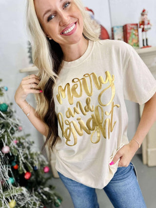 Woman wearing a 'Merry and Bright' shirt in a festive setting with a Christmas tree.