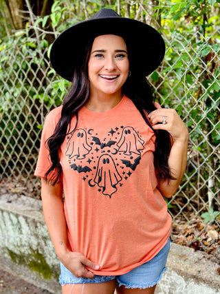 Woman wearing a coral t-shirt with black graphics and a black hat, standing outdoors.