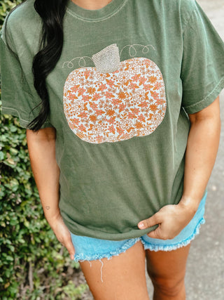 Person wearing a green t-shirt with a floral pumpkin design, standing outdoors.