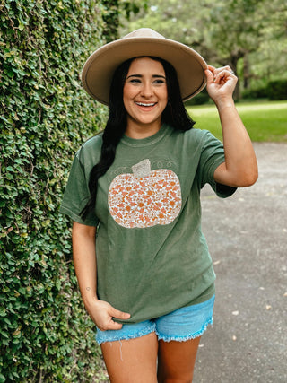 Woman wearing a green t-shirt with a floral pumpkin design, standing outdoors.